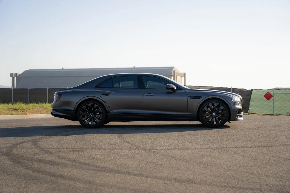 Full side profile of the matte gray Flying Spur with dark wheels and window trim.