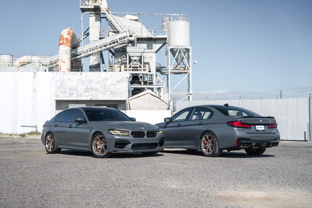 Two gray BMW M5 CS sedans positioned together, one facing forward and the other showing its rear three-quarter angle