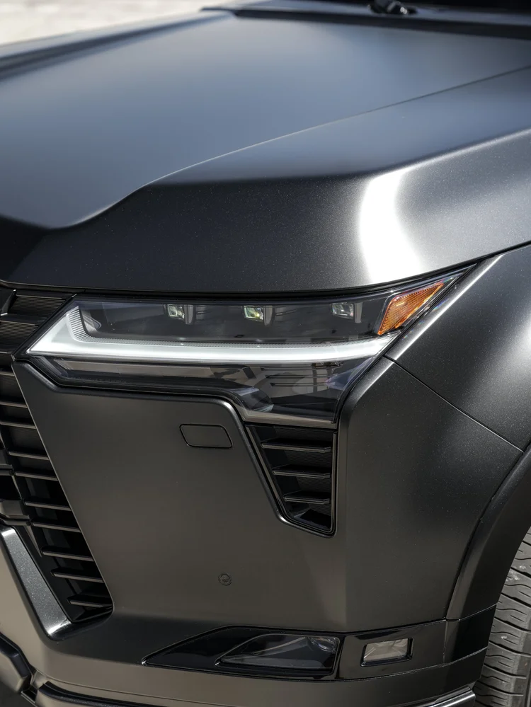 Opposite headlamp close-up with a bright white light strip, amber outer element and a strong highlight along the dark hood ridge
