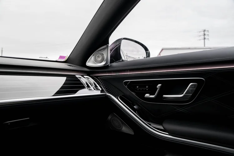 Passenger-door and dashboard detail with a silver-colored speaker, seat-shaped controls, stitched dark trim and a thin pink light strip