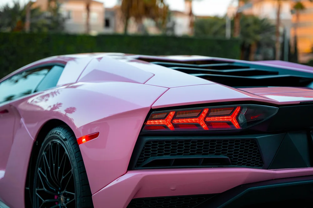 Sakura Pink Aventador rear quarter with a red taillight, black grille and reflections across the pink fender