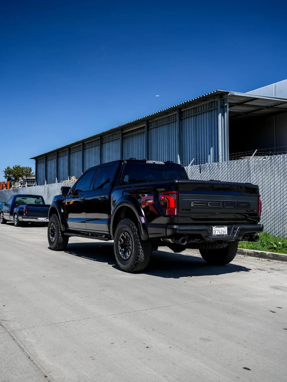 Rear three-quarter view of the black Ford F-150 Raptor R beside an industrial fence.