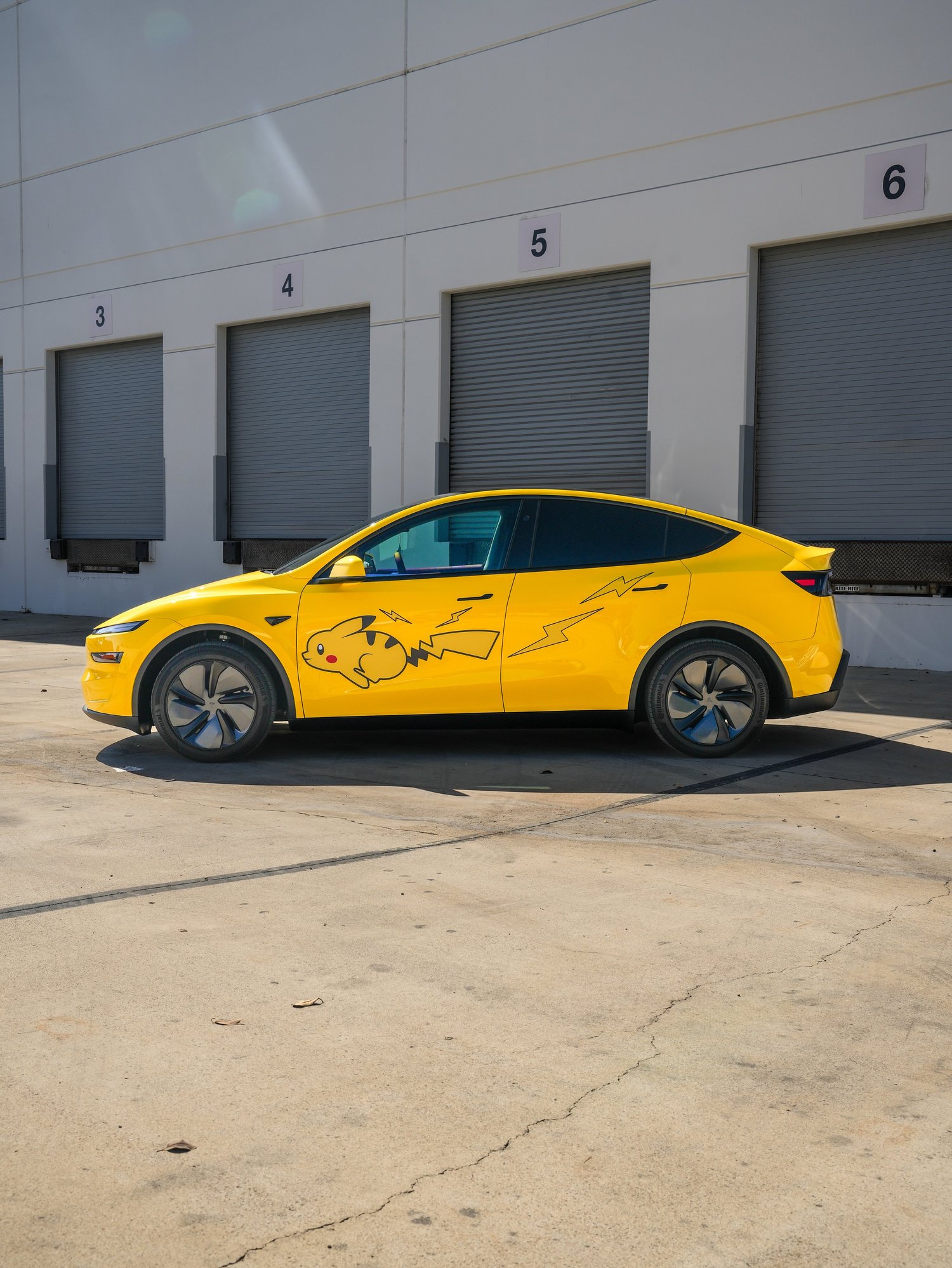 Tesla Model Y with Vegas Yellow vinyl wrap and Pikachu graphics, driver-side profile