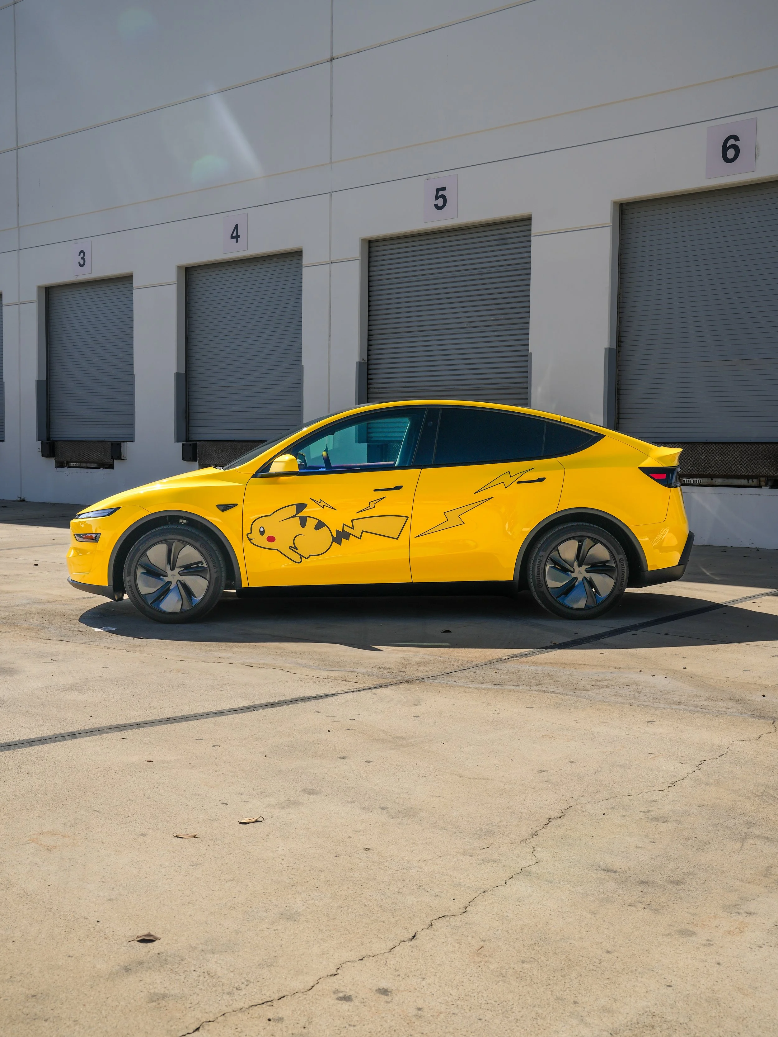 Tesla Model Y with Vegas Yellow vinyl wrap and Pikachu graphics, driver-side profile