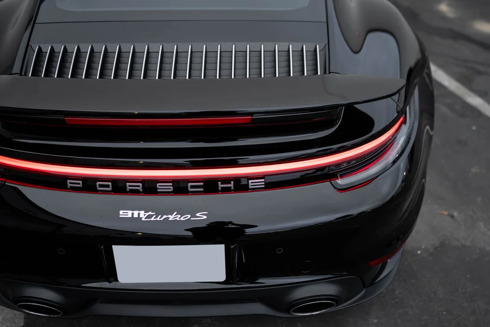High rear view of the black Porsche 911 Turbo S showing spoiler, vent slats, light bar and badge