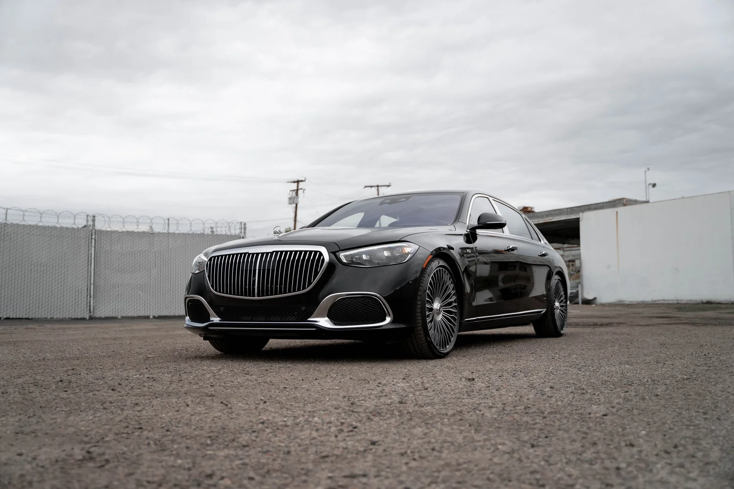 Complete low opposite front-three-quarter view of the black S 680 with silver multispoke wheels and a bright grille beside a gray fence