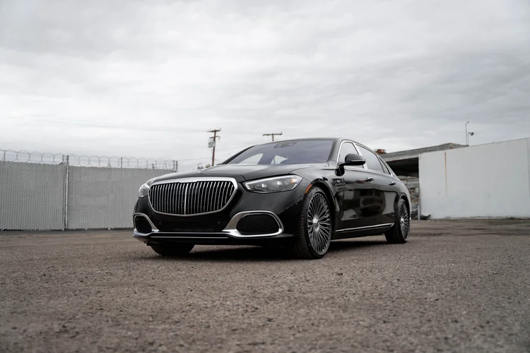 Complete front three-quarter view of a black Mercedes-Maybach S 680 with a bright vertical grille, hood ornament and silver-colored multispoke wheels on gravel.