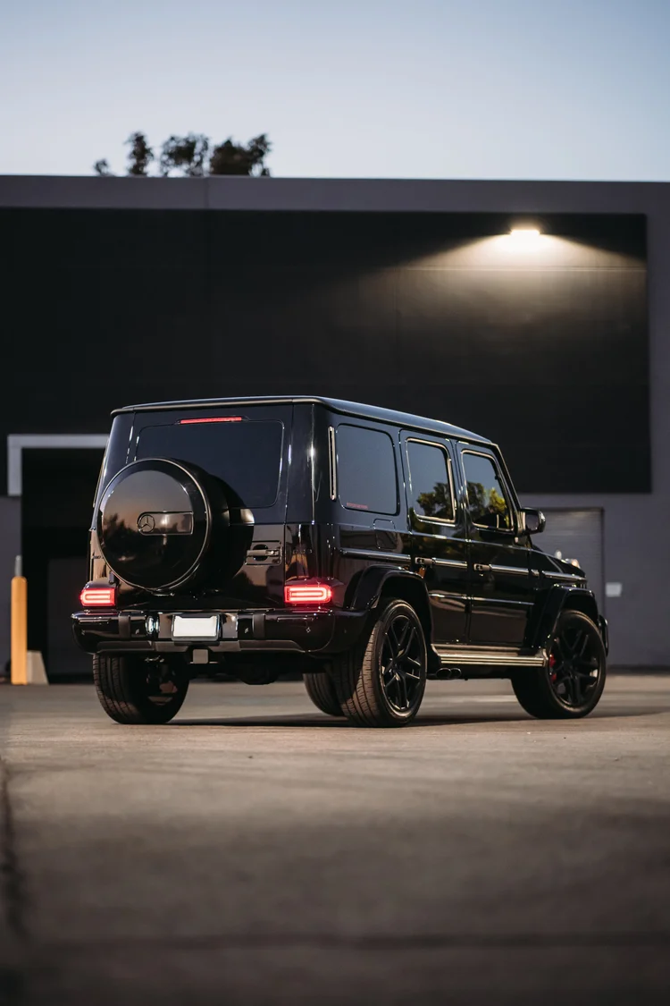 Complete dark G 63 in a tall rear three-quarter frame, with illuminated red rear lamps and a circular spare-wheel cover.