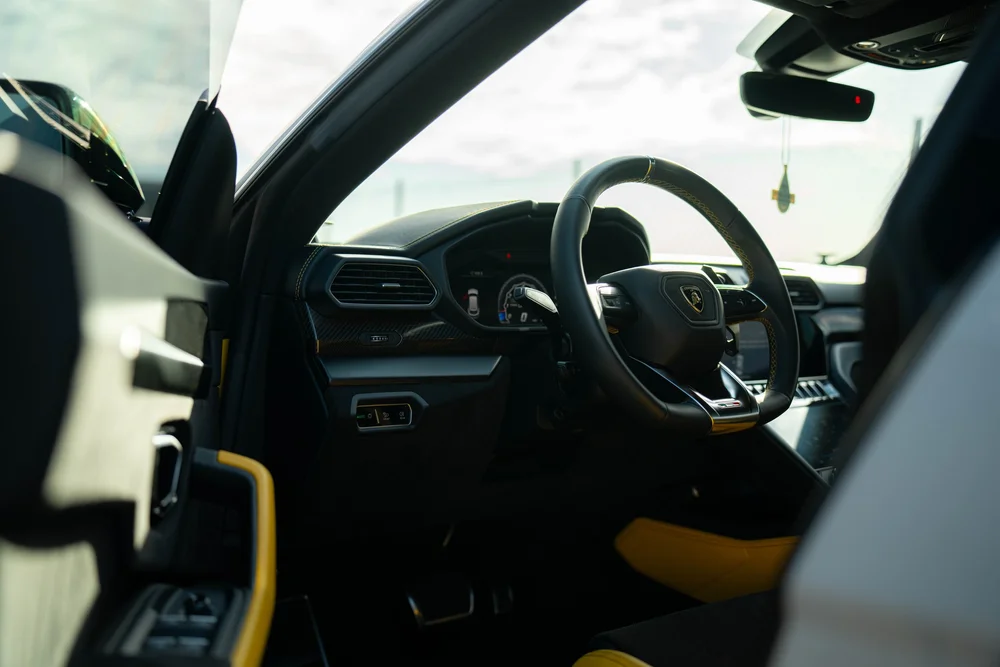 Lamborghini Urus with Chalk vinyl wrap, cockpit view through the open driver door with steering wheel and dashboard
