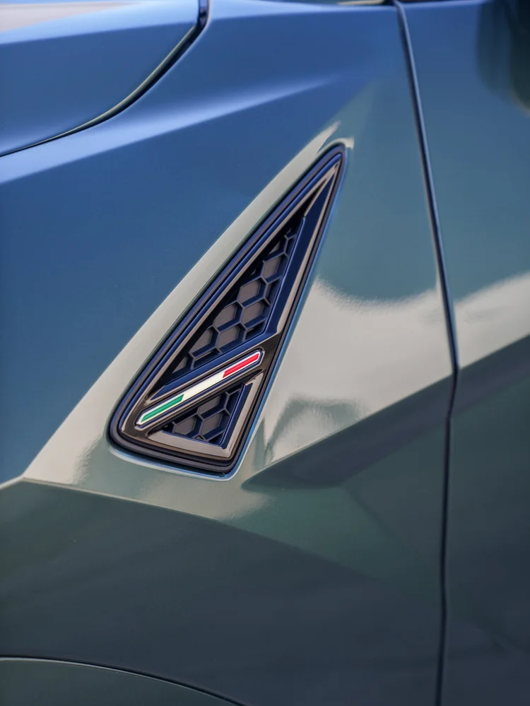 Close triangular front-fender vent of the green Lamborghini Urus S with black honeycomb mesh and a green, white and red Italian tricolor accent.