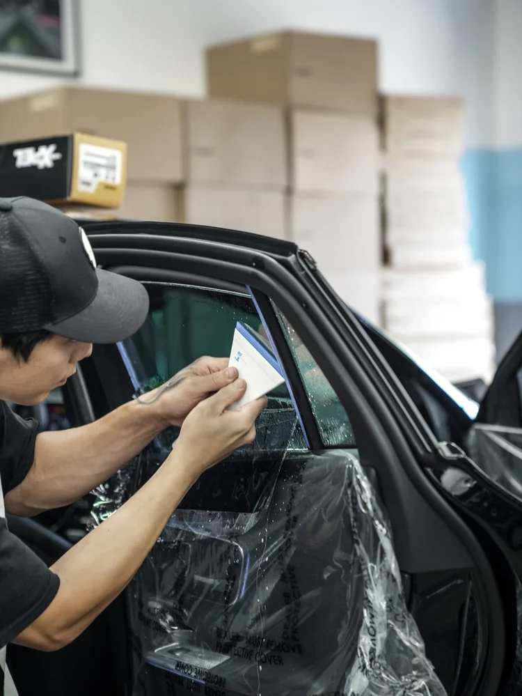 Close view of a technician using a white and blue flat tool against wet side-window film on the Mercedes-AMG GLC 63 S, with a transparent protective door cover below.