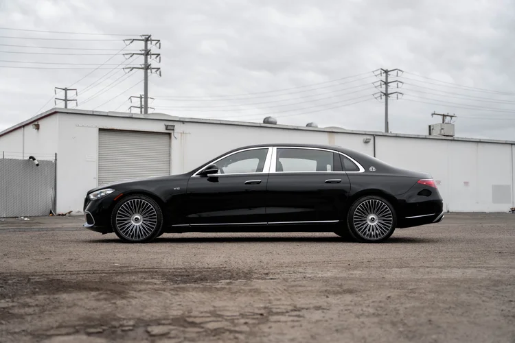 Complete side profile of the black S 680 with bright window surrounds and silver multispoke wheels beside a pale industrial building