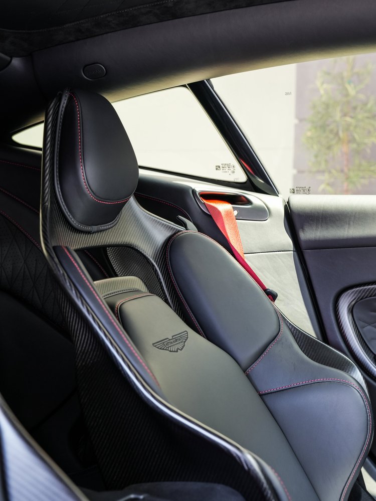 DB12 front seat with red stitching, a red seat belt and weave-pattern shell beside side glass.