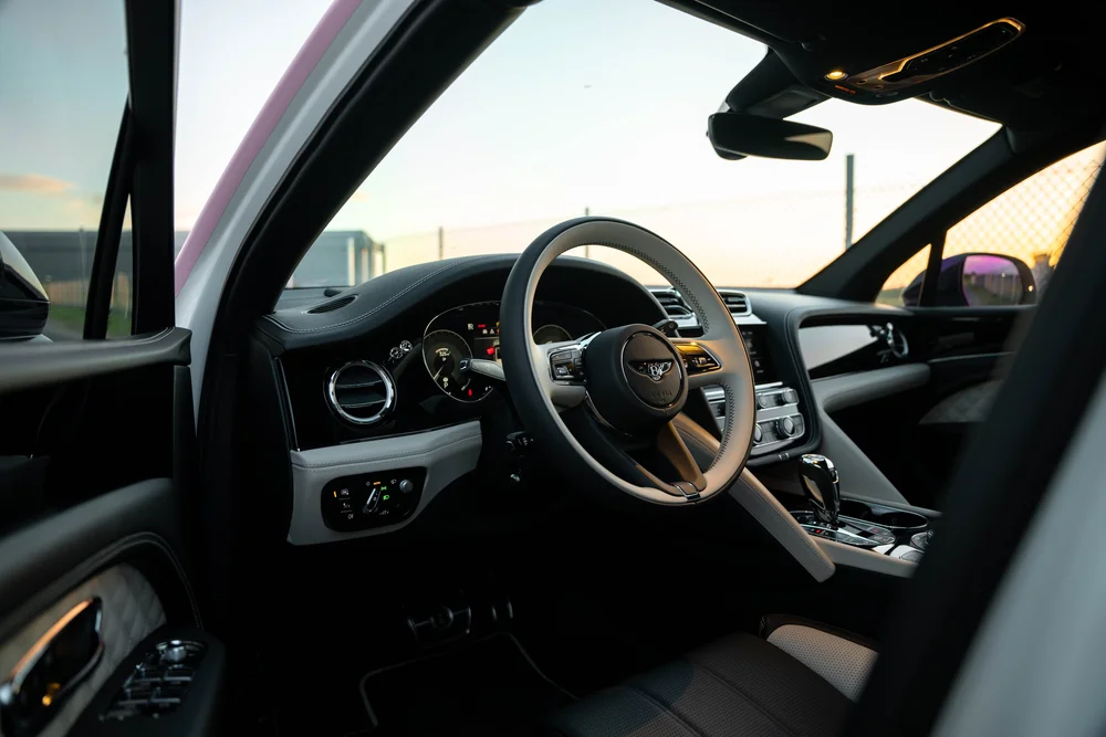Bentayga driver cabin viewed through the open door, with the Bentley steering-wheel emblem, dashboard and circular vents visible