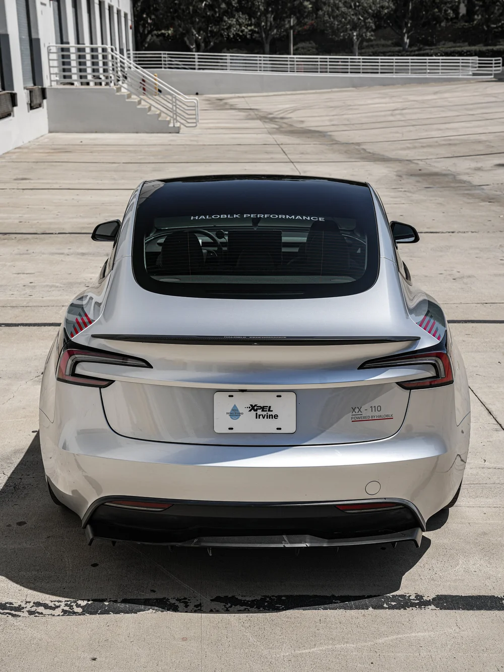 Centered rear view of the silver Model 3 with HALOBLK rear-glass lettering, a dark spoiler, tail lights and graphic bumper details.