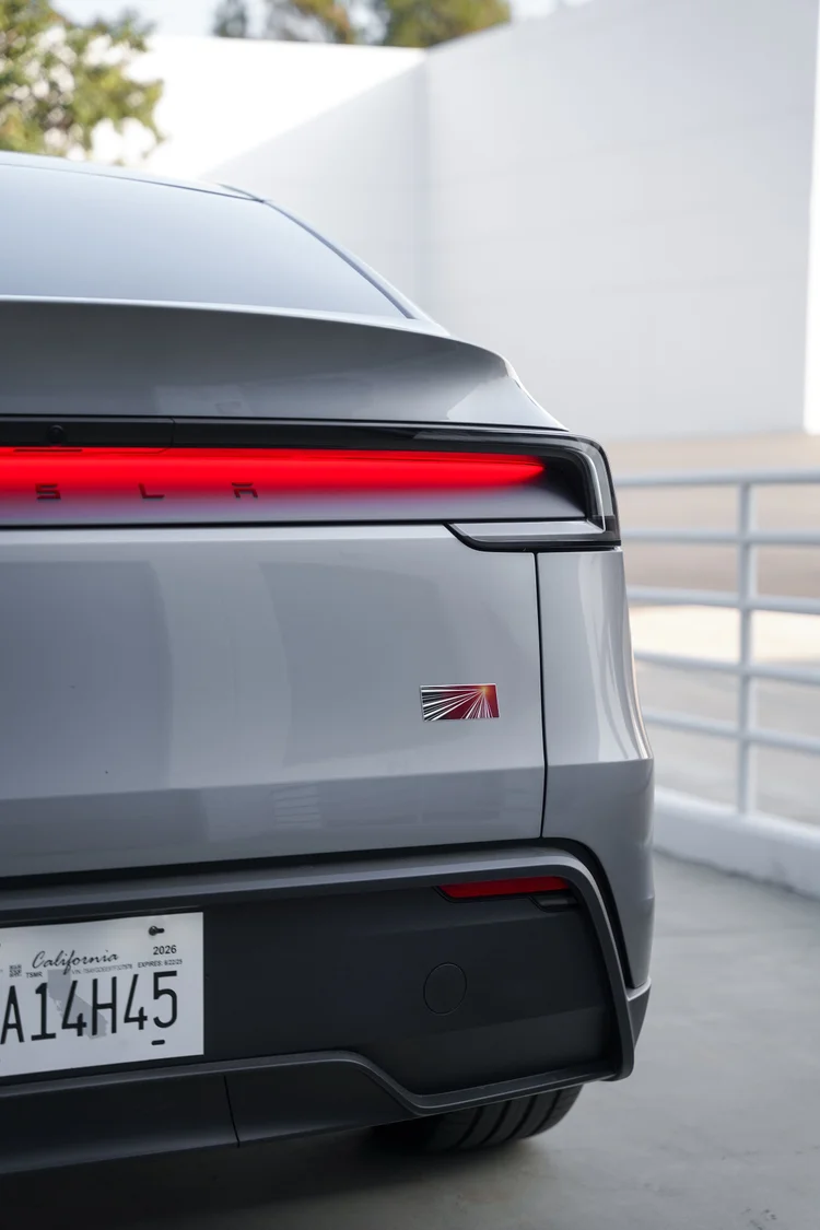 Close-up of the Tesla Model Y rear corner with the red light bar, gray liftgate, spoiler and dark lower bumper.