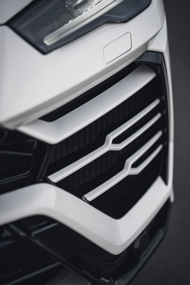 Portrait front-corner detail showing the headlamp, white bumper creases and black intake with light horizontal accents.
