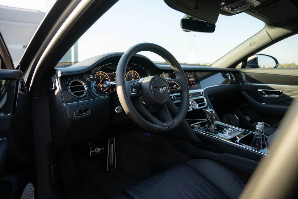 Open-door view into the dark cabin with steering wheel, round vents and center console.