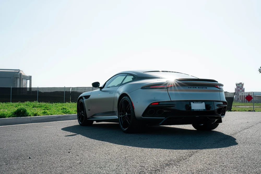 Matte-finish Aston Martin DBS in a low rear three-quarter view with sunlight across the rear roofline