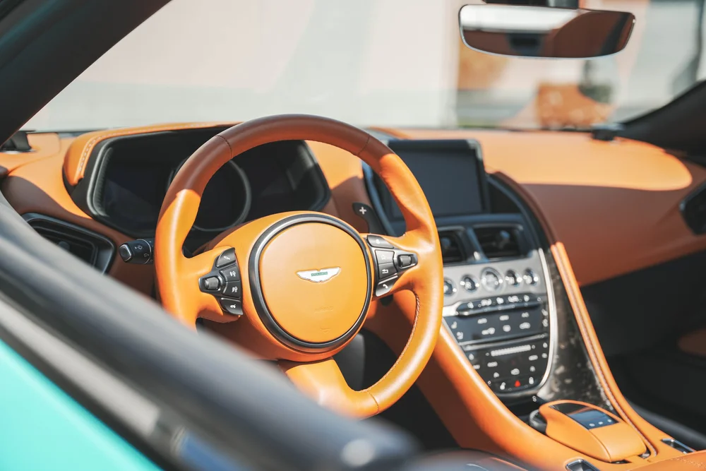 Orange DB11 steering wheel, dashboard and centre console viewed through the open-roof cabin