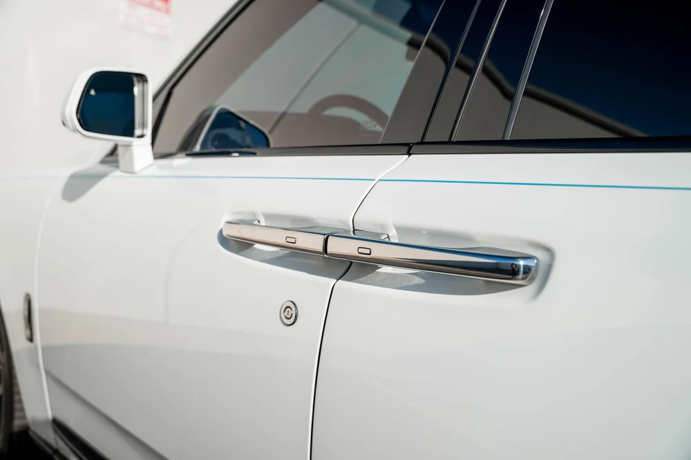 White Rolls-Royce Cullinan — chrome door handle, thin turquoise coachline and adjacent white bodywork