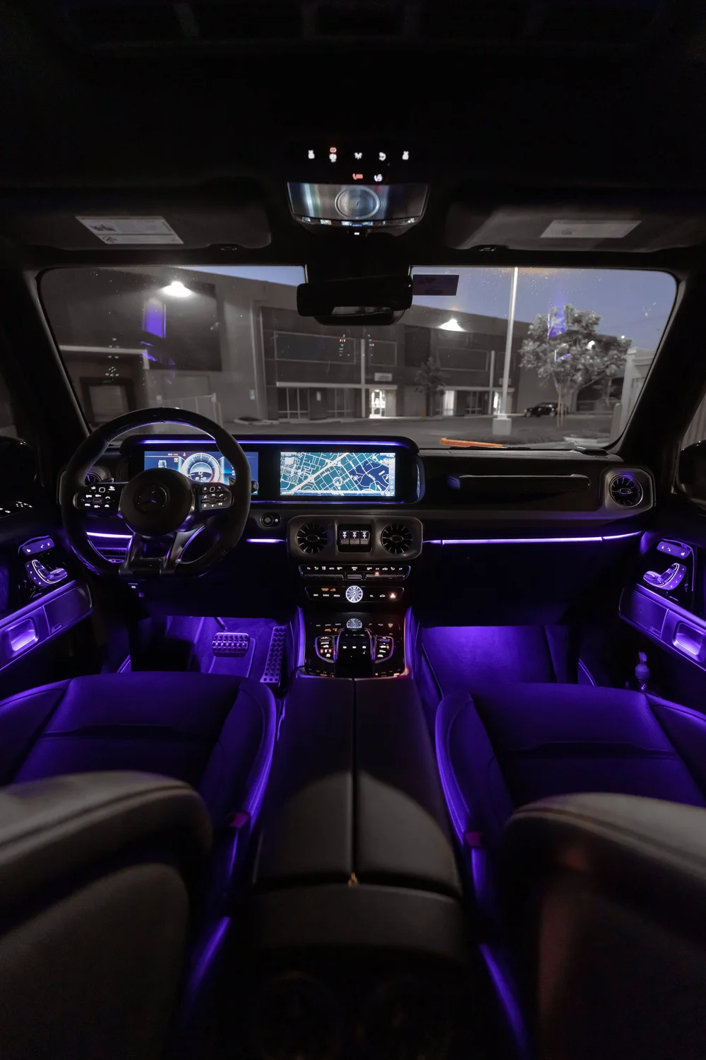Dark cabin with purple accent lighting across the dashboard, doors and footwells, beside illuminated gauges and a map screen.