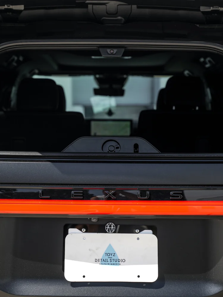 Rear detail through the raised rear glass with dark seat backs, LEXUS tailgate lettering, a red light bar and a Toyz Detail Studio display plate