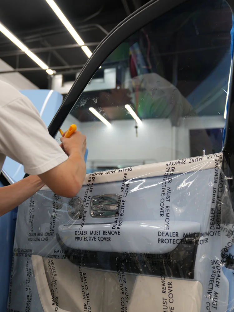 Technician pressing Cullinan side-window film with a yellow tool above protective covering on the open door