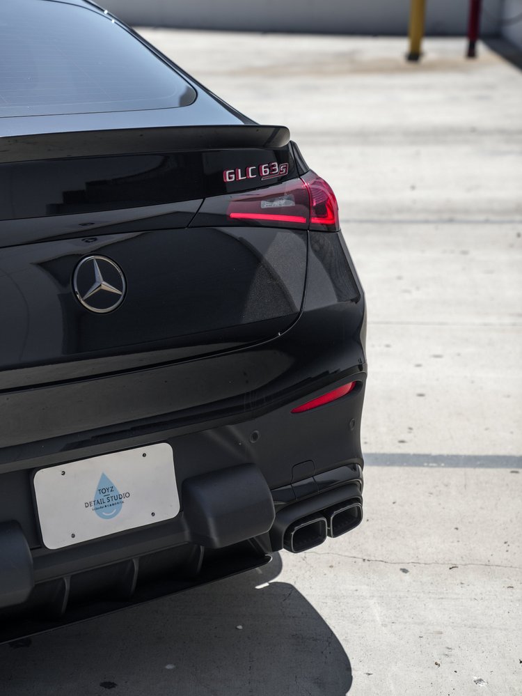 Close rear view of the black Mercedes-AMG GLC 63 S showing GLC 63 S lettering, a red taillight, Mercedes star, Toyz plate and two rectangular exhaust outlets.