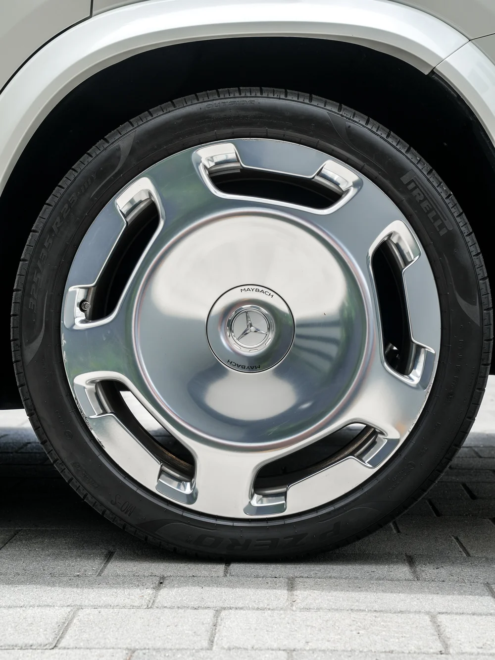 Polished disc-style Maybach wheel with black openings, a center emblem and black tire beneath the white wheel arch.