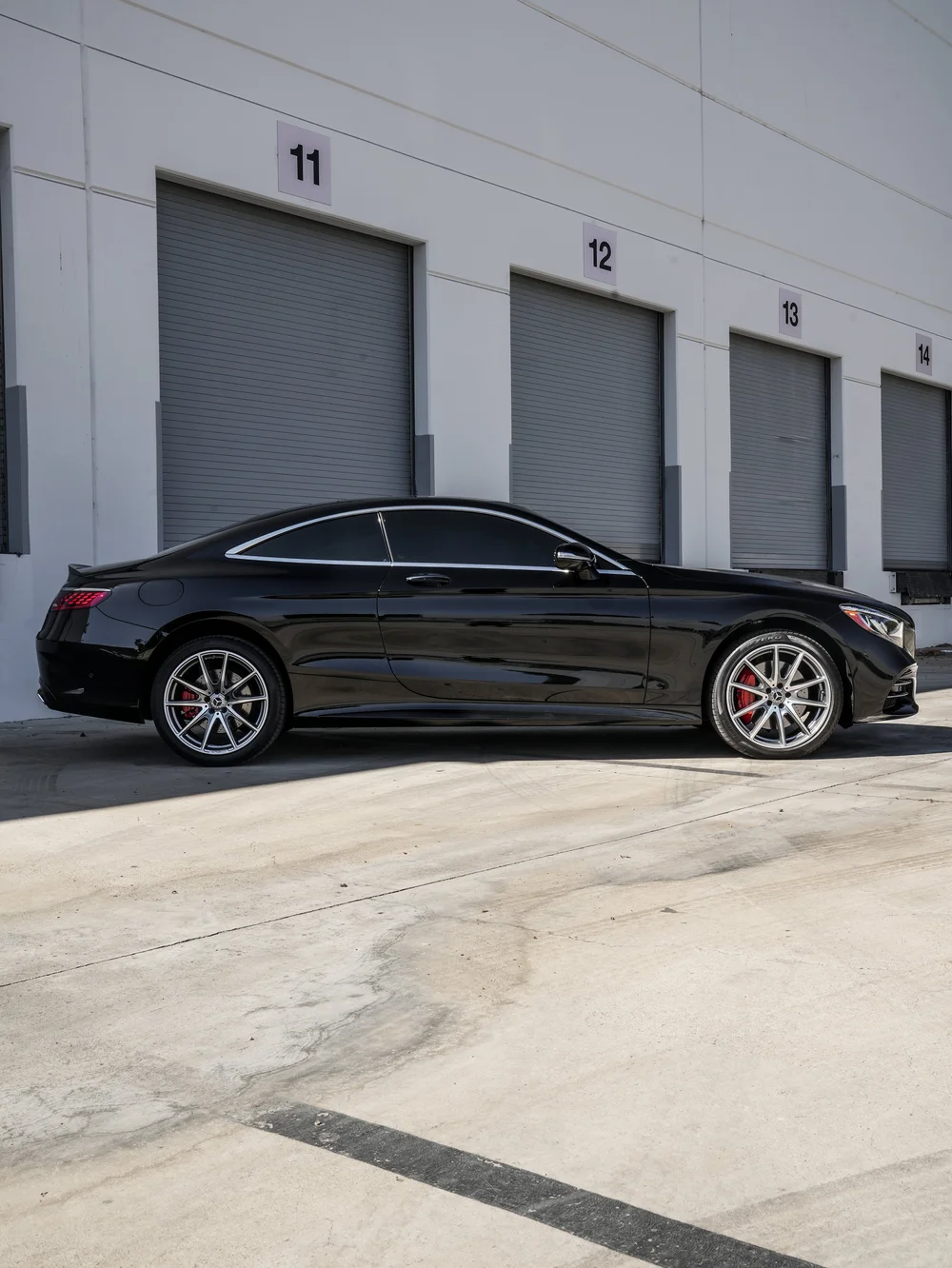 Complete side profile of the glossy black Mercedes-Benz S 560 coupe facing right, with silver multi-spoke wheels, red brake calipers and a bright window surround.
