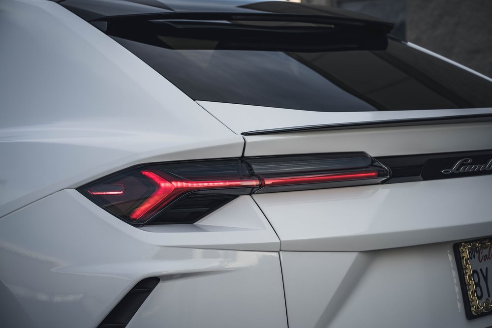 Close rear-lamp view with red Y-shaped light, white body creases and a black trim strip below the rear glass.