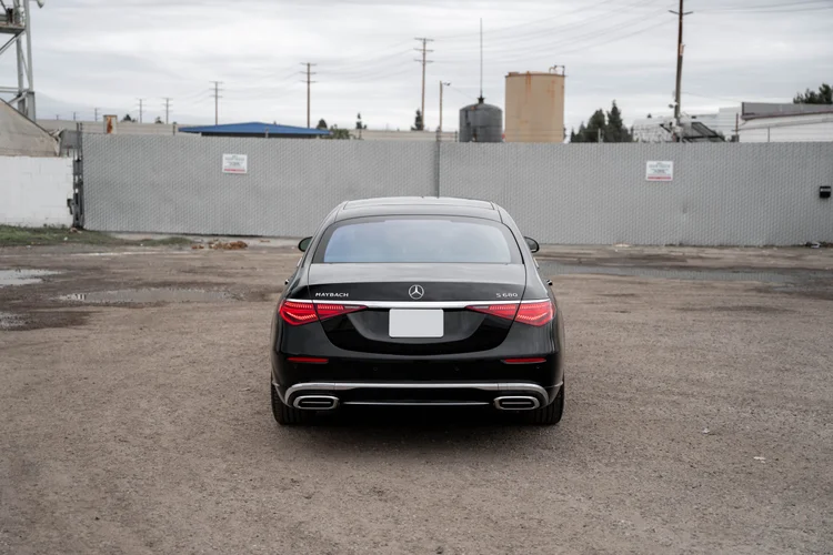 Complete higher rear view of the S 680 centered below a gray fence with red lamps, bright trunk trim and both exhaust surrounds