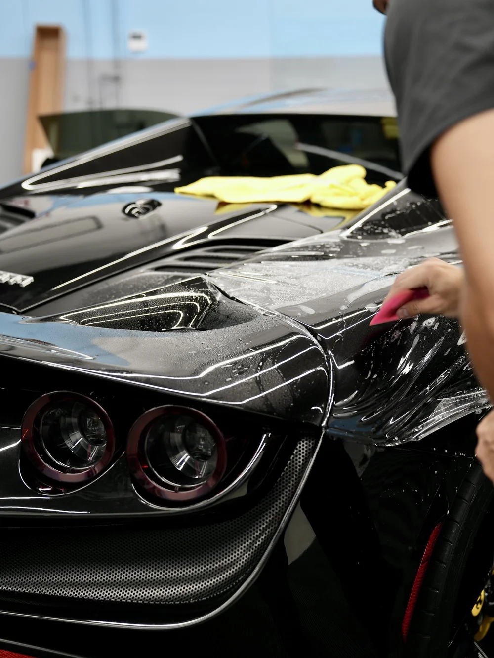 Technician applying paint protection film to the hood of a black exotic car