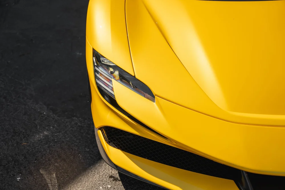 Close view of the yellow Ferrari SF90 headlamp, hood seam and black mesh front air opening