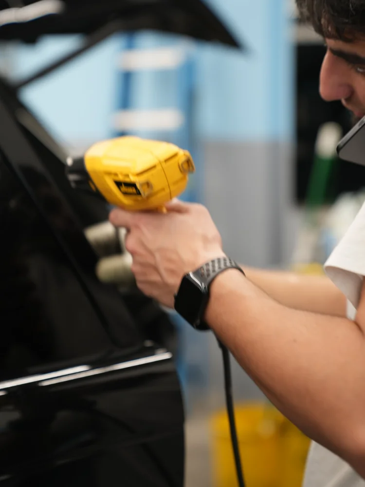 Technician holding a yellow heat gun beside the Range Rover’s dark window and door trim.