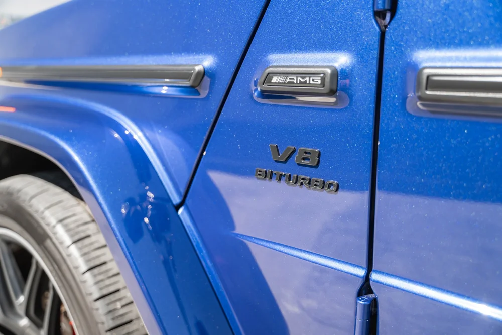 Close-up of the AMG plaque and V8 BITURBO lettering on the reflective blue G 63 fender beside a door hinge