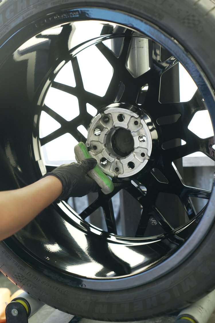 Gloved hand holding a cloth against the inner side of a removed dark BMW wheel with its mounting face visible.