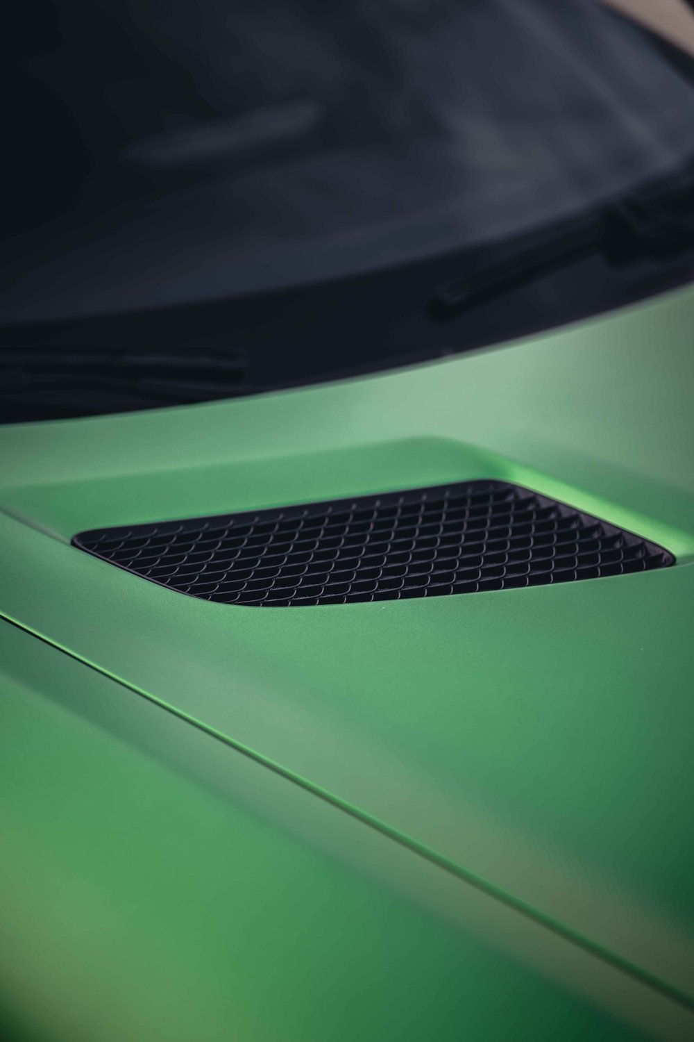 Black mesh hood vent set into matte green bodywork below the dark windshield.