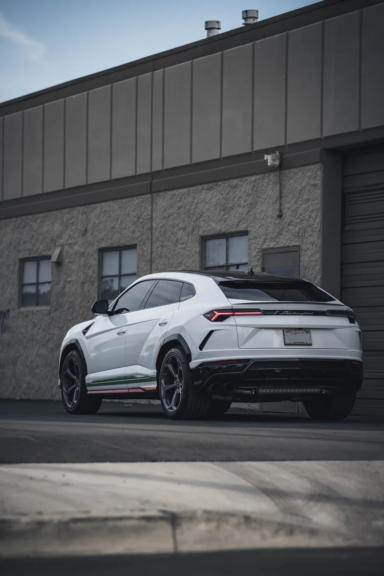 Complete white Urus in a tall rear three-quarter frame, with red rear lamps and green, white and red lower-side bands.