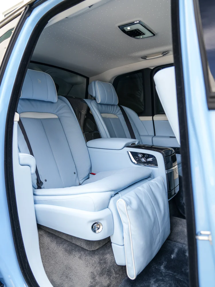 Pale blue Cullinan rear seats, center armrest and extended footrest seen through the open rear door