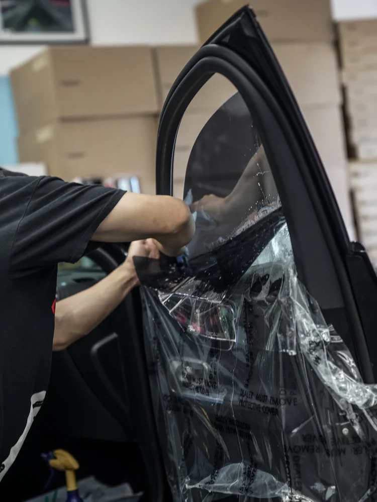 Technician working at wet film on an open Mercedes-AMG GLC 63 S side window, with the door trim covered by a transparent protective sheet.