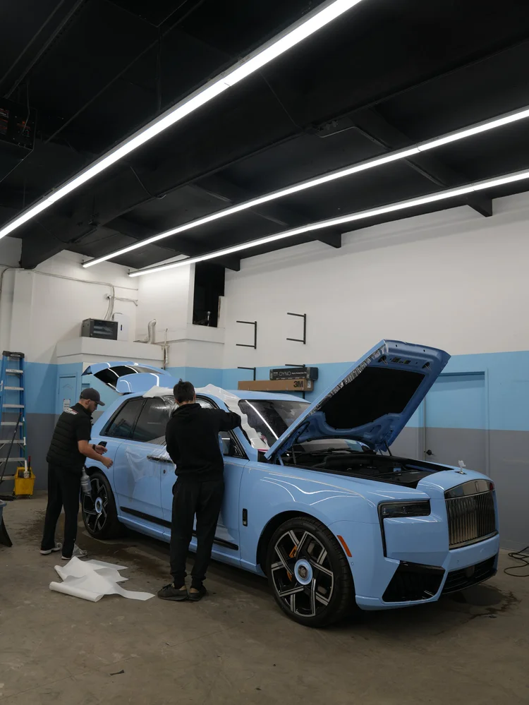 Powder Blue Cullinan inside the Toyz studio with its hood open and two technicians beside the side bodywork