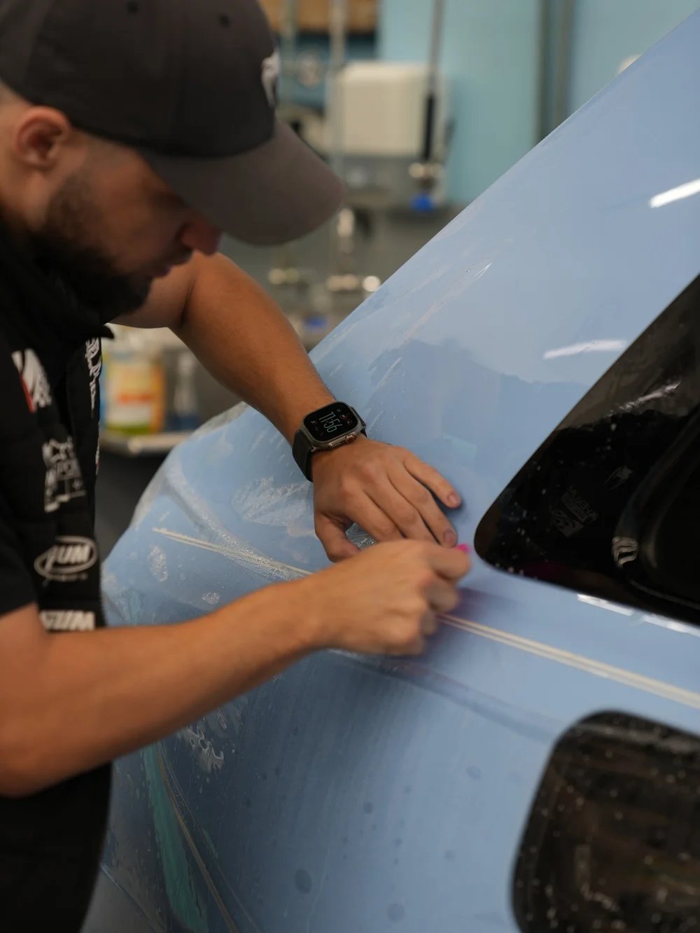 Toyz technician smoothing clear paint protection film over the Powder Blue Cullinan rear quarter beside its gold coachline