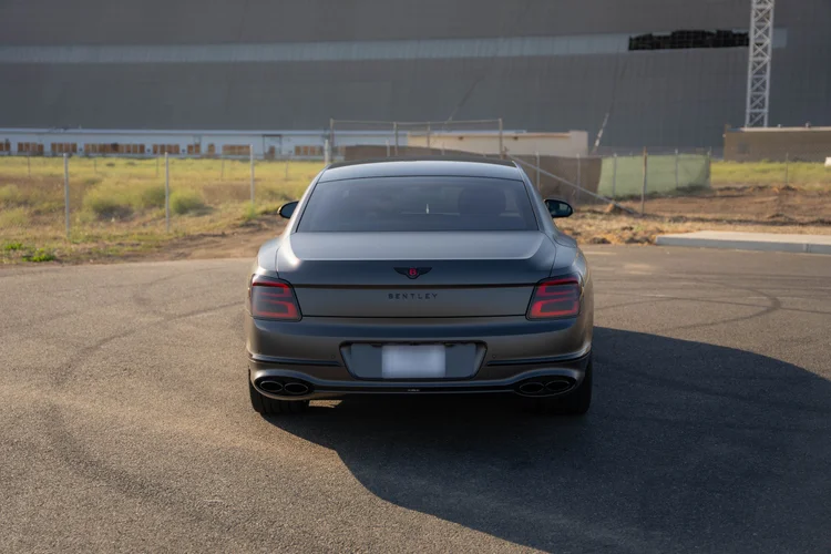 Complete centered rear view of the sedan with its shadow stretching across the pavement.