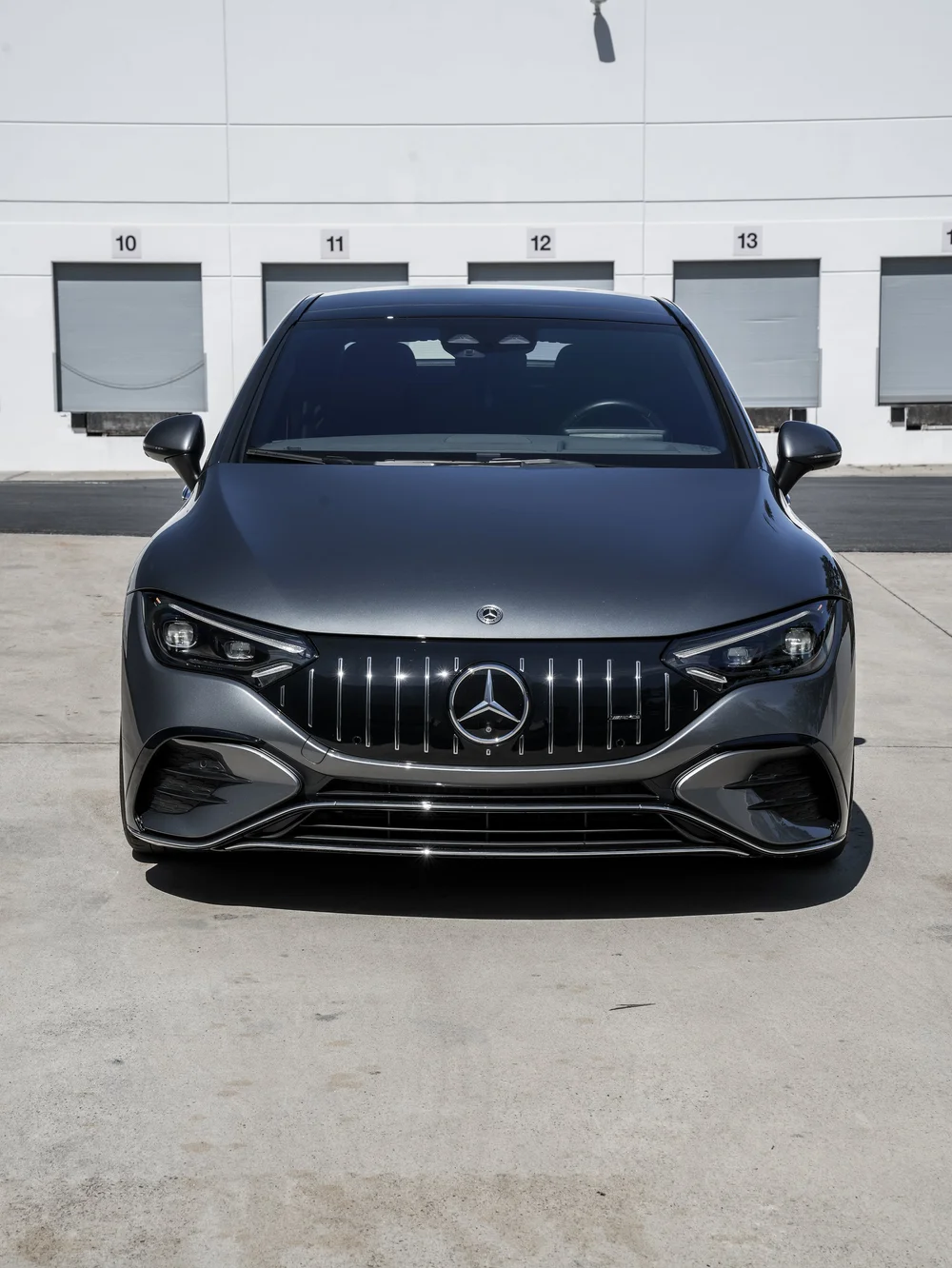 Straight front view of the gray Mercedes-AMG EQE 53 showing the roof, mirrors, headlamps and star grille.