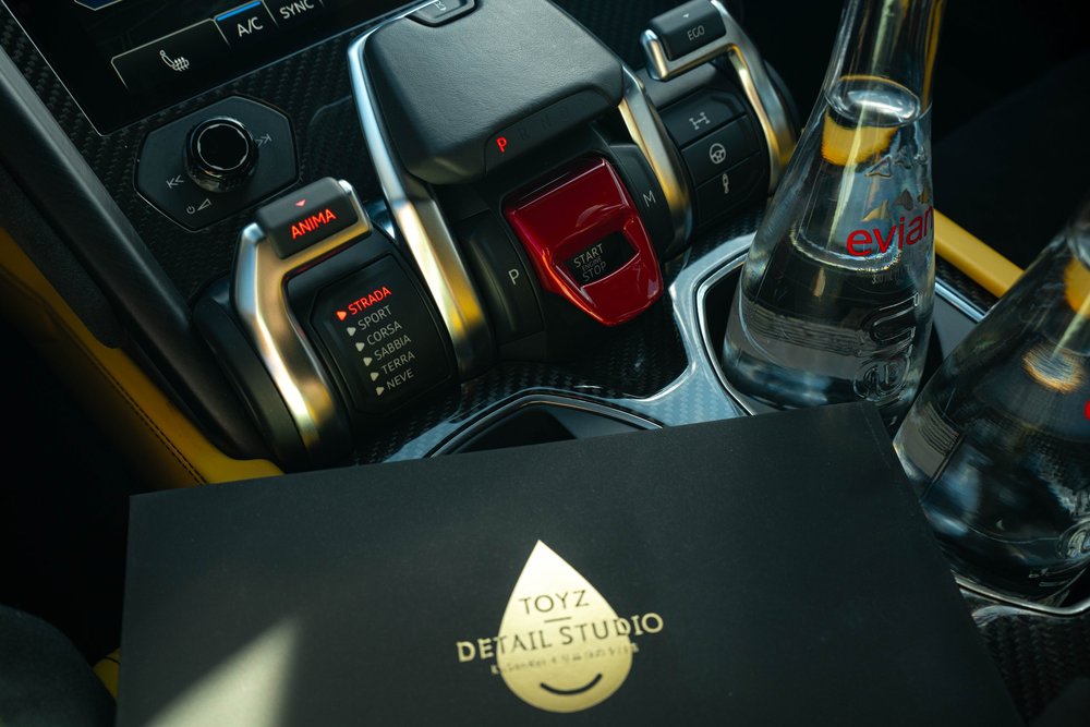 Lamborghini Urus with Chalk vinyl wrap, center-console start button and drive-mode controls beside a Toyz booklet