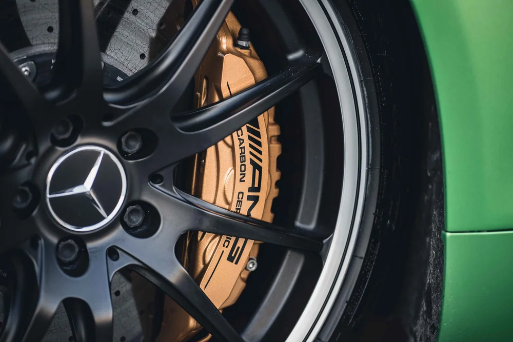 Gold-toned caliper with visible AMG lettering behind dark wheel spokes and a Mercedes star center cap.