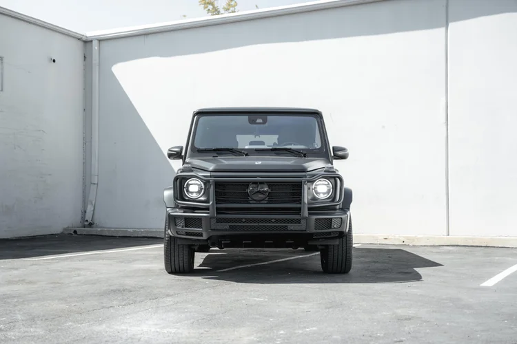 Complete straight front view of the grey G 550 with bright circular headlamps and a dark front guard beside a white wall