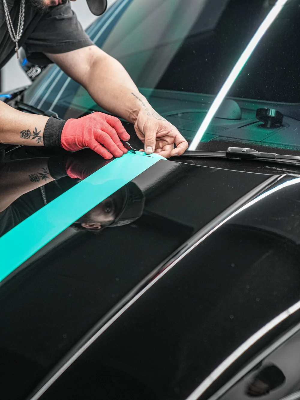 Close view of a technician finishing the turquoise hood graphic near the windshield on the Porsche 911 Carrera 4 GTS